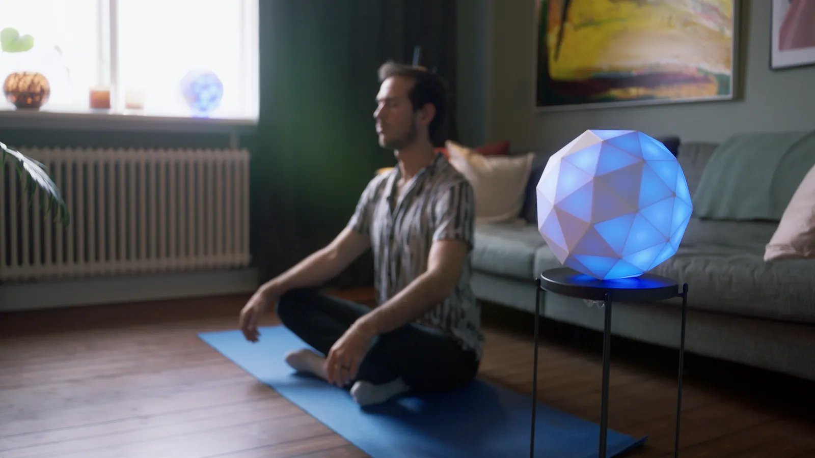 Eine blau leuchtende GLORB neben einem Mann, der auf einer Yogamatte meditiert