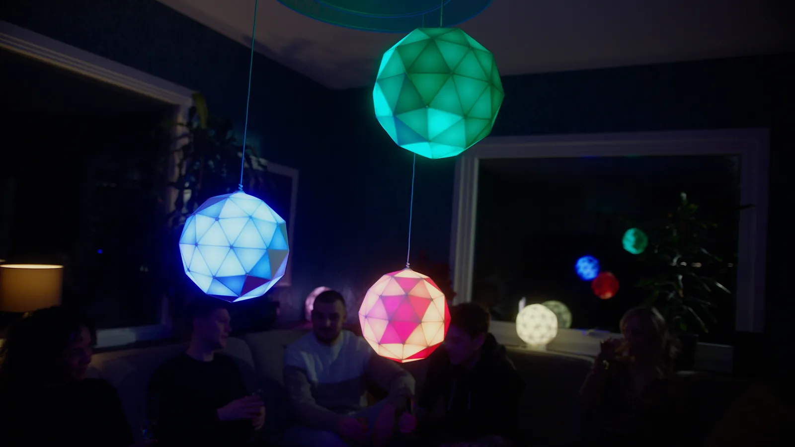 Drei GLORBs in Grün, Blau und Rot hängen als Pendelleuchten über einer Wohnzimmerrunde